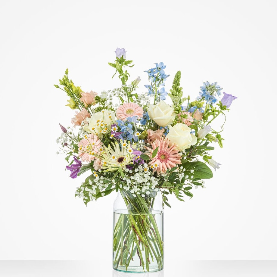 Groot boeket met een mix van bloemen zoals roze gerbera’s, witte rozen, en blauwe ridderspoor in een glazen vaas.