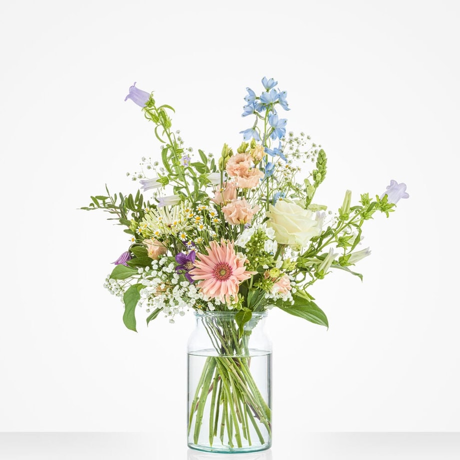 Klein boeket met delicate bloemen in pastelkleuren, waaronder rozen, gerbera’s, en andere veldbloemen, geplaatst in een glazen vaas.
