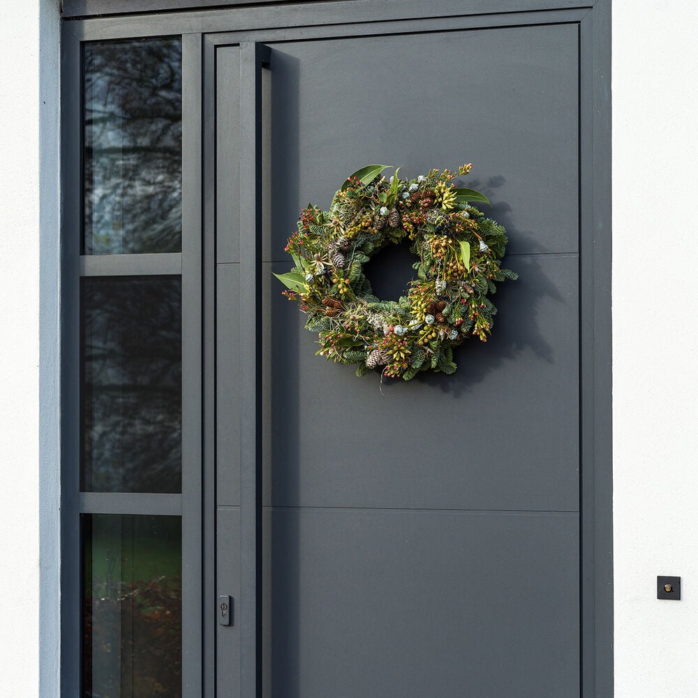 Luxe kerstkrans met dennen, bessen en eucalyptus op een voordeur.