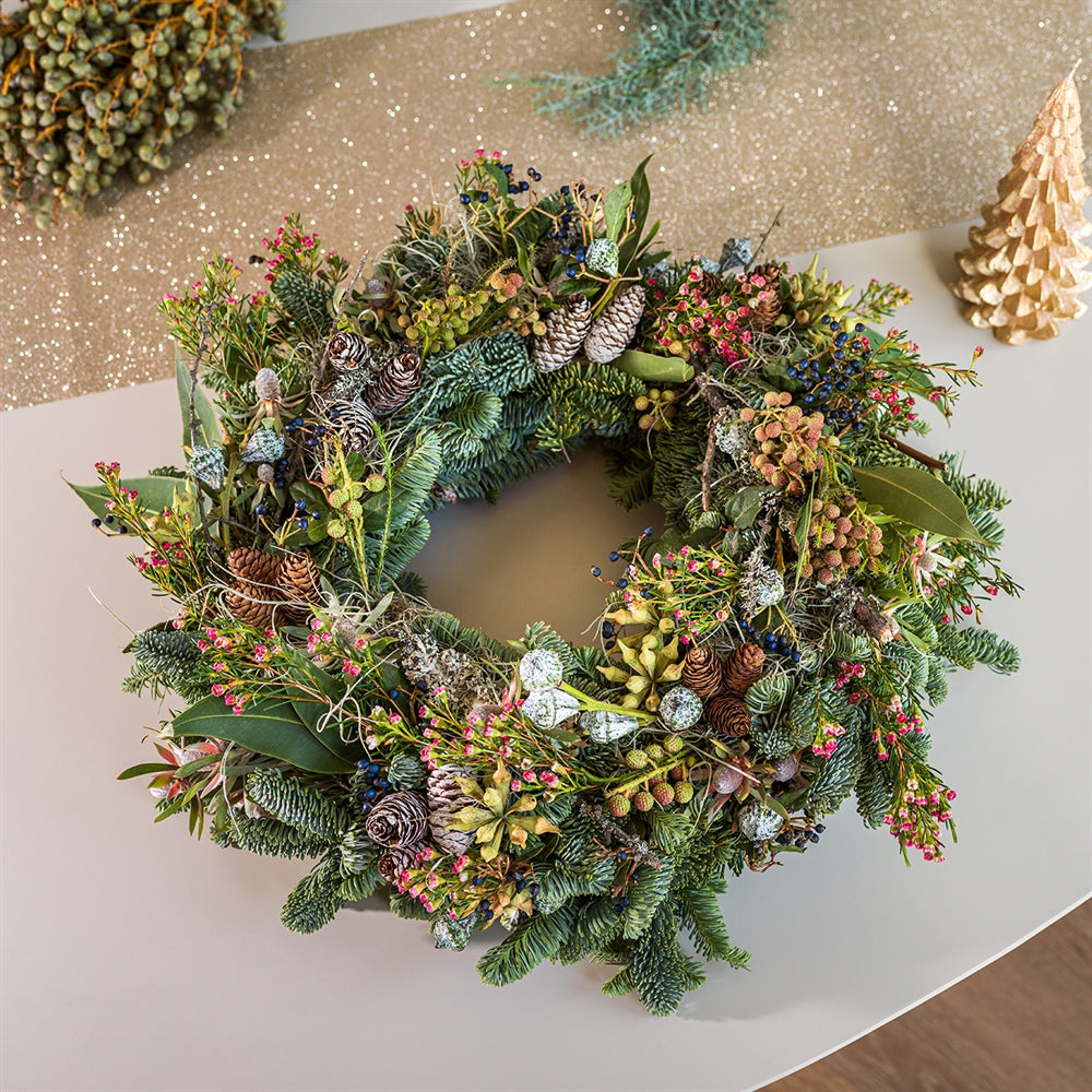 Luxe kerstkrans met dennengroen, dennenappels en kleurrijke decoratie op een feestelijk versierde tafel.