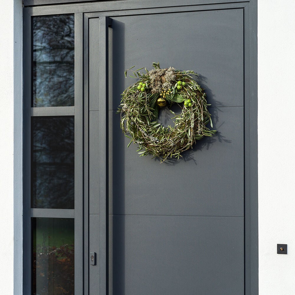 Groene kerstkrans met decoratie aan een moderne grijze voordeur.