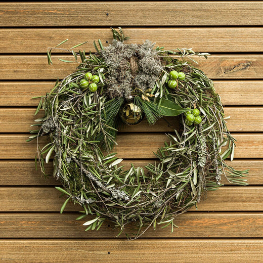 Groene kerstkrans met mos en decoratieve takken tegen een houten achtergrond.