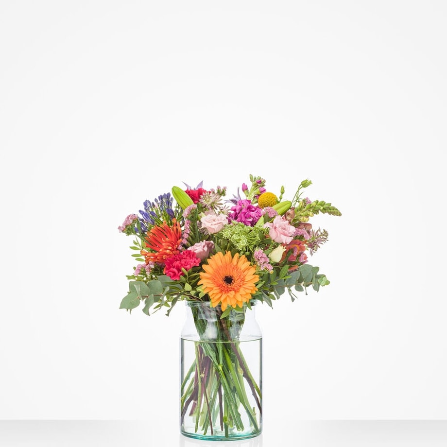 Klein boeket met een levendige mix van bloemen, waaronder gerbera’s, rozen en veldbloemen in felle tinten, in een glazen vaas.