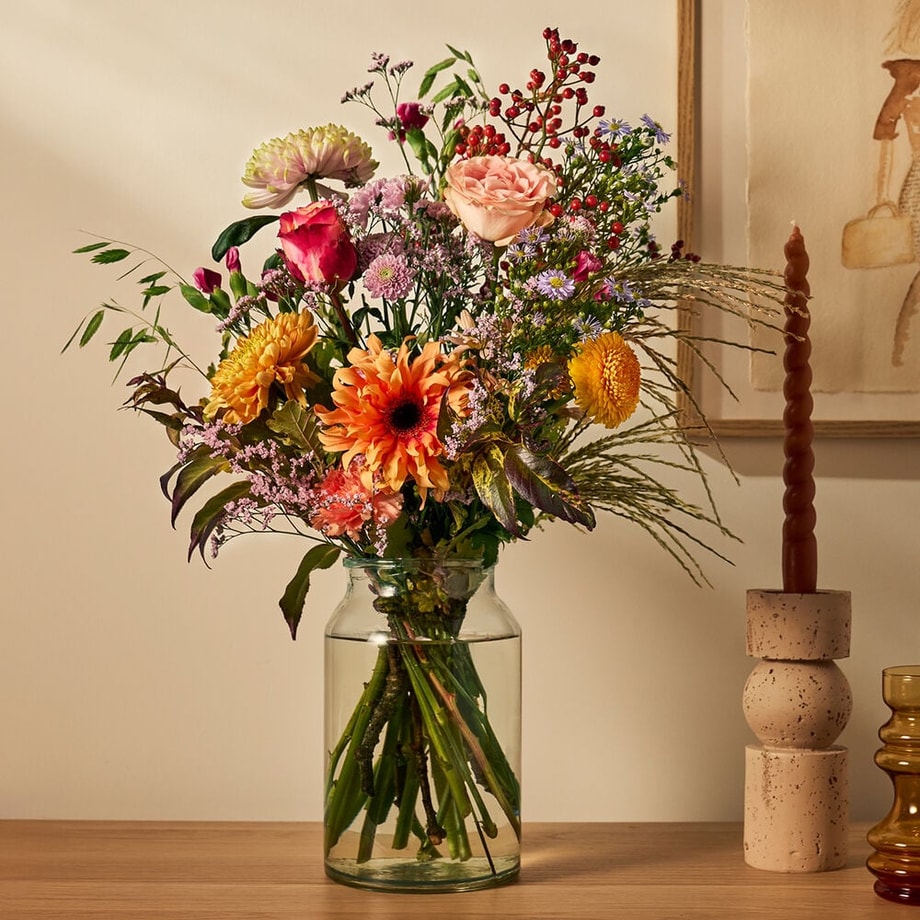Herfstboeket met oranje gerbera’s, rozen en besjes in glazen vaas. Warme kleuren voor in huis.