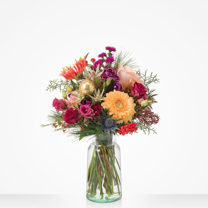 Kerstboeket met oranje gerbera, roze rozen en paarse bloemen in glazen vaas.