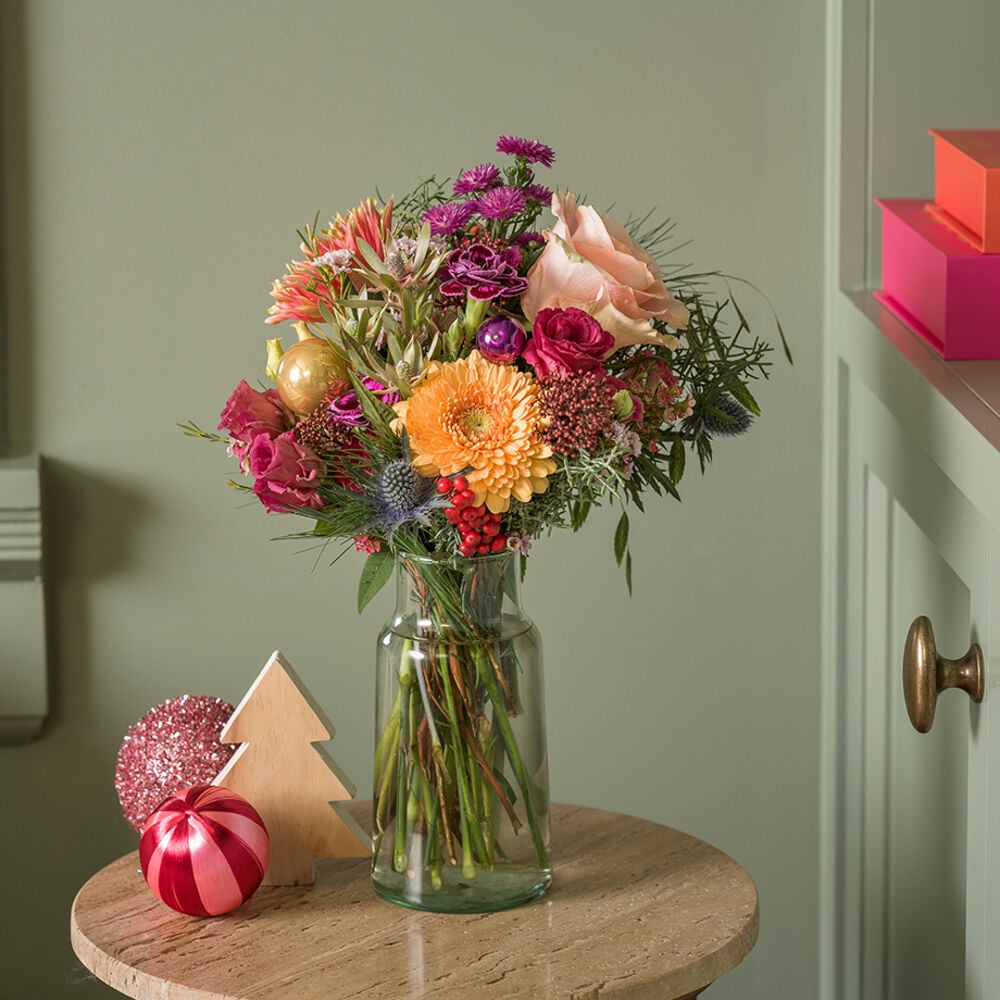 Kerstboeket met kleurrijke winterbloemen in glazen vaas in een feestelijke setting.