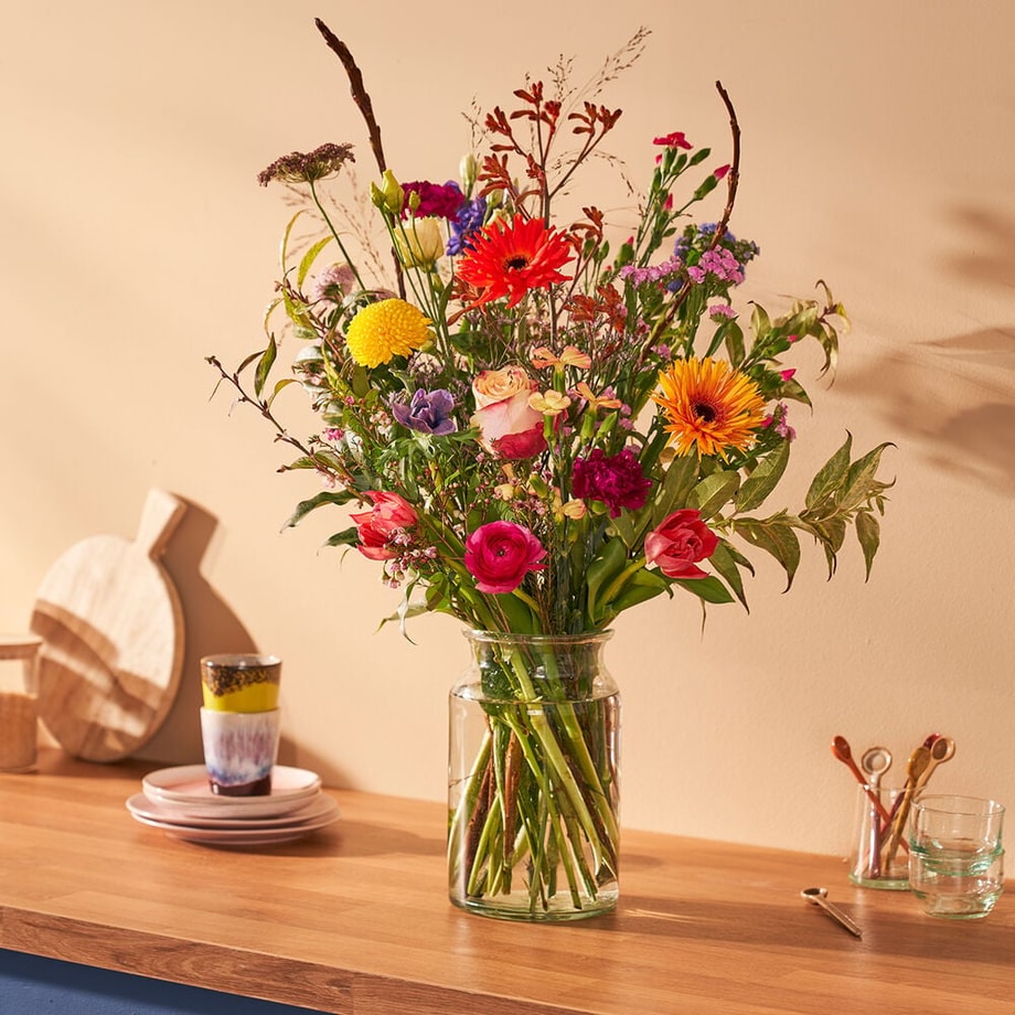 Kleurrijk lenteboeket met lentebloemen in een glazen vaas op een houten tafel.