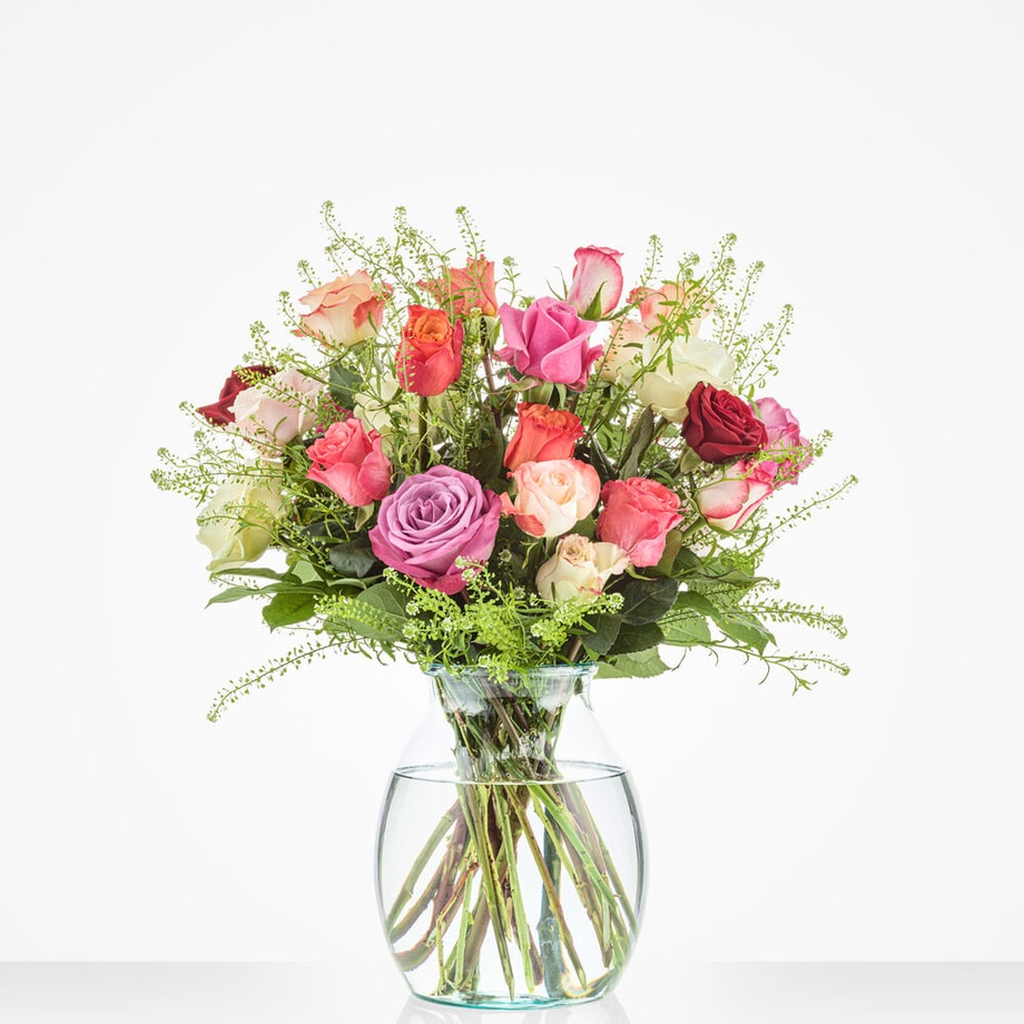 Groot boeket van kleurrijke rozen in verschillende tinten zoals rood, roze, wit en lila, gecombineerd met groene bladeren in een glazen vaas.