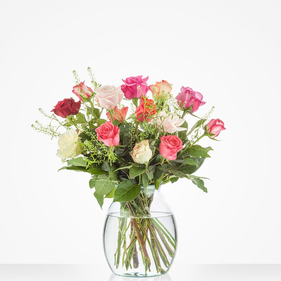 Klein boeket van rozen in zachte tinten, waaronder roze, wit en rood, in een elegante glazen vaas.