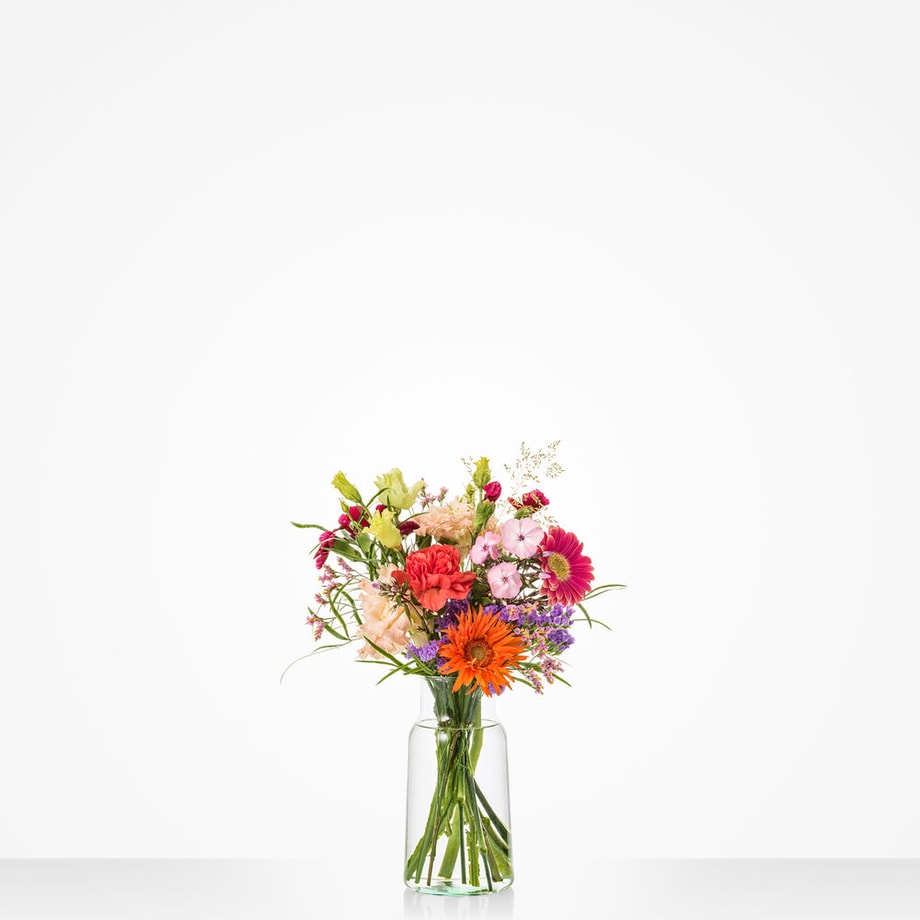 Klein boeket in een glazen vaas van 18 cm met een mix van kleurrijke bloemen zoals oranje gerbera’s, rode rozen, en paarse bloemen.