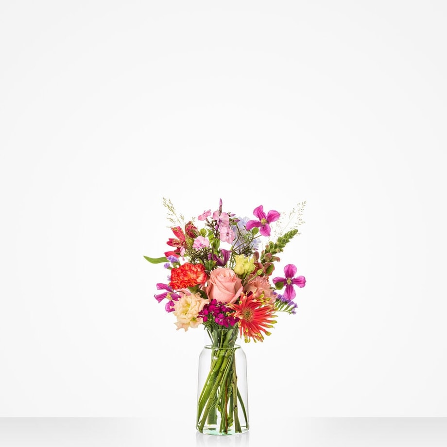 Middelgroot boeket met diverse bloemen, waaronder roze rozen, paarse en oranje gerbera’s, in een glazen vaas van 18 cm.