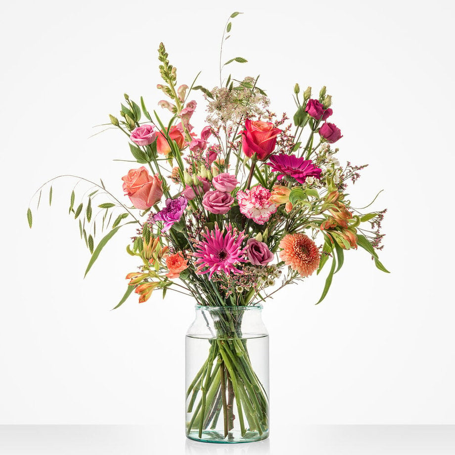 Groot boeket met roze en oranje bloemen zoals rozen, gerbera’s en lisianthus in een glazen vaas
