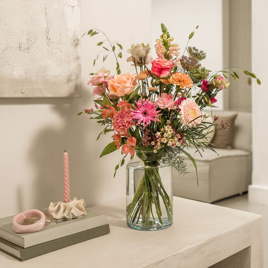 Zacht roze boeket met gerbera’s, rozen en anjers in een glazen vaas.