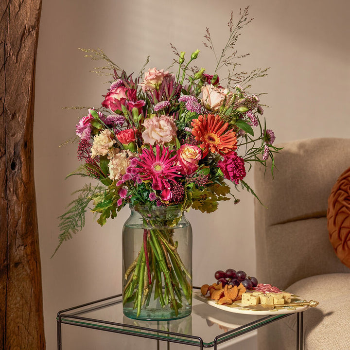 Herfstboeket in roze en oranje tinten met seizoensbloemen, sfeervol op tafel gepresenteerd naast borrelplank.