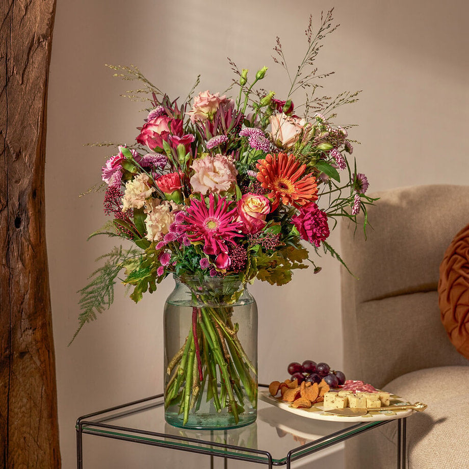 Herfstboeket in roze en oranje tinten met seizoensbloemen, sfeervol op tafel gepresenteerd naast borrelplank.