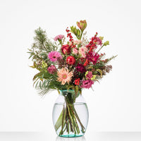 Klein kerstboeket met rozen, gerbera’s en rode kerstballen in glazen vaas.