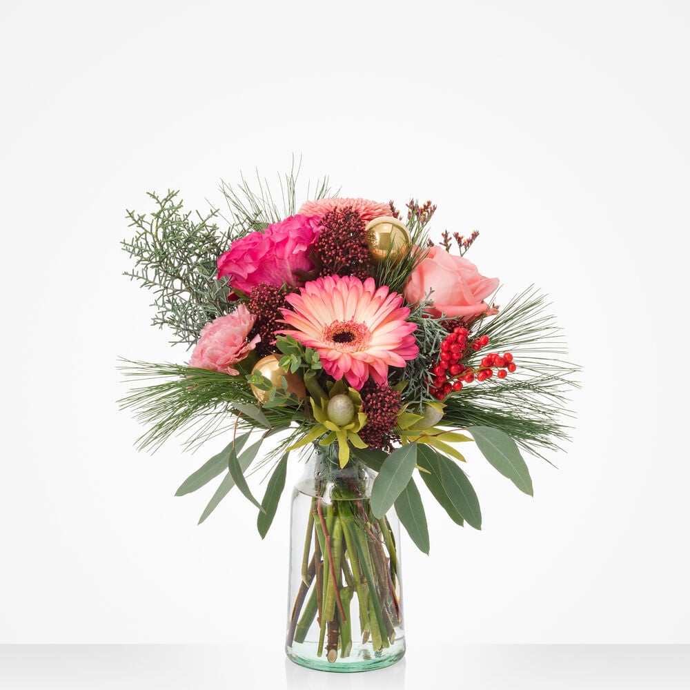 Kerstboeket met roze gerbera, rozen en wintergroen in glazen vaas.