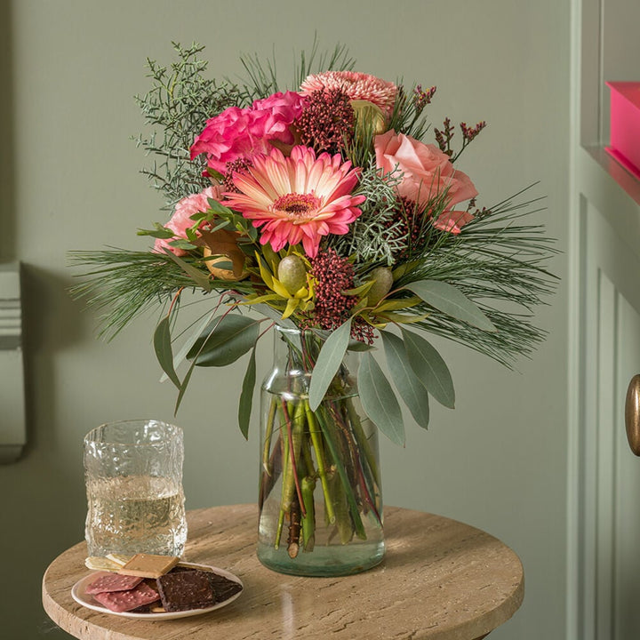 Kerstboeket met roze gerbera en rozen in glazen vaas in een warm interieur.