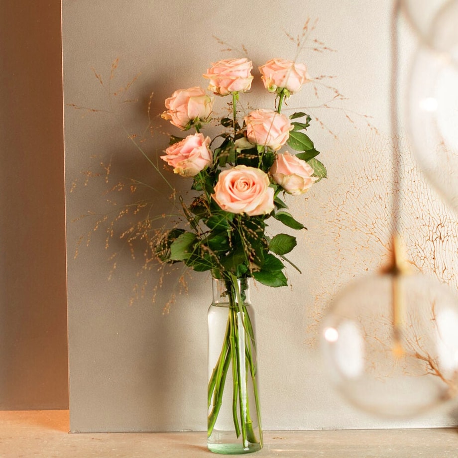 Roze rozen in een smalle glazen vaas tegen een wit-gouden achtergrond.