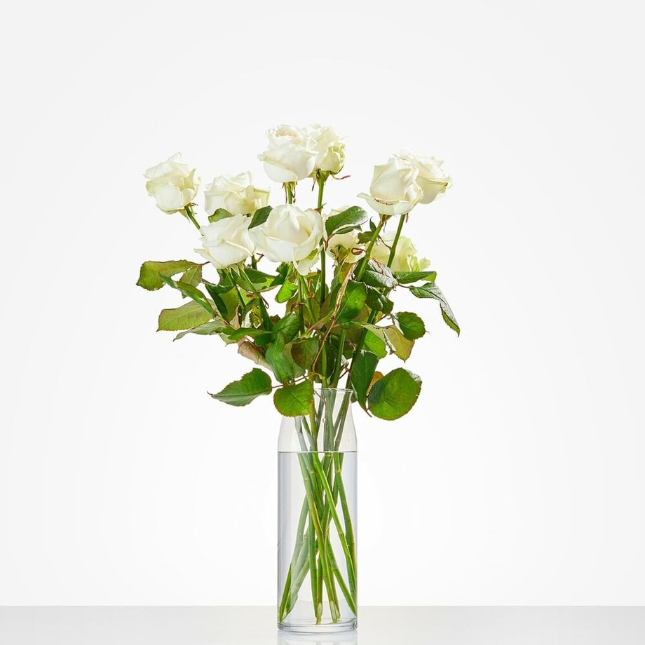 Witte rozen in een elegante glazen vaas met groene bladeren.
