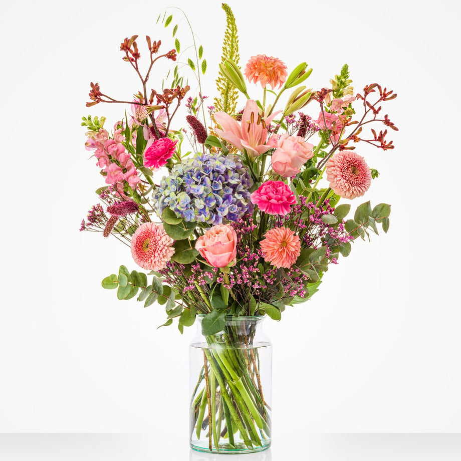 Groot maandboeket augustus met een mix van seizoensbloemen zoals dahlia’s, hortensia’s, gerbera’s en rozen in een glazen vaas.