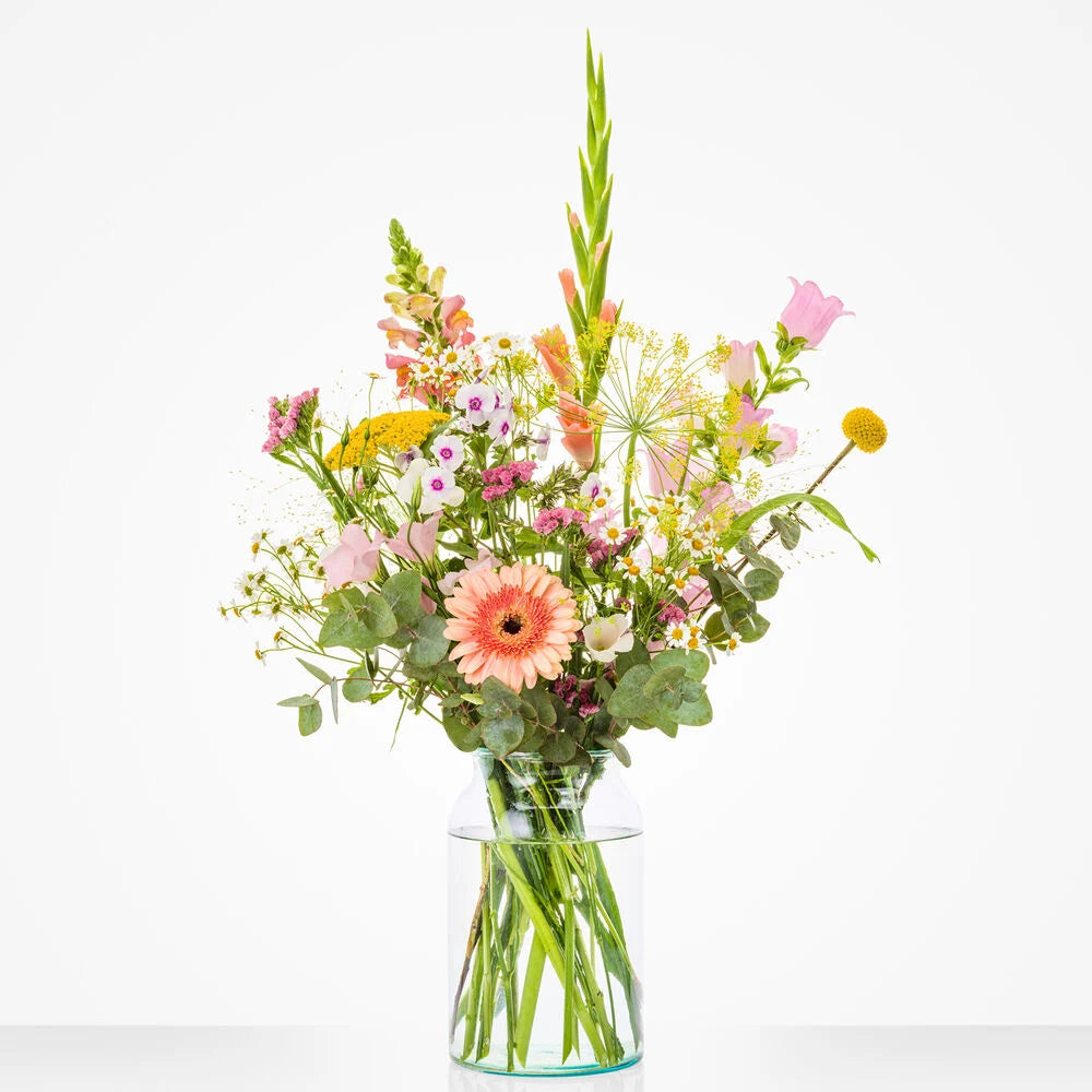 Klein maandboeket juli met zomerse veldbloemen zoals gele craspedia’s, roze campanula’s, en kamille in een glazen vaas.