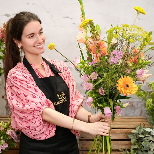 Bloemist met het maandboeket juli, met kleurrijke zomerbloemen zoals lelies, gerbera’s, en dille.