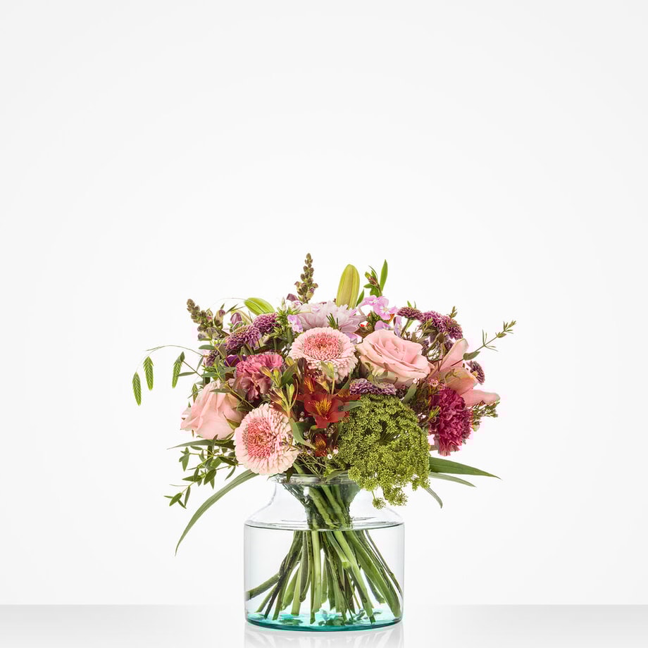 Middelgroot boeket met roze en bordeaux bloemen, waaronder rozen en chrysanten, in glazen vaas tegen witte achtergrond