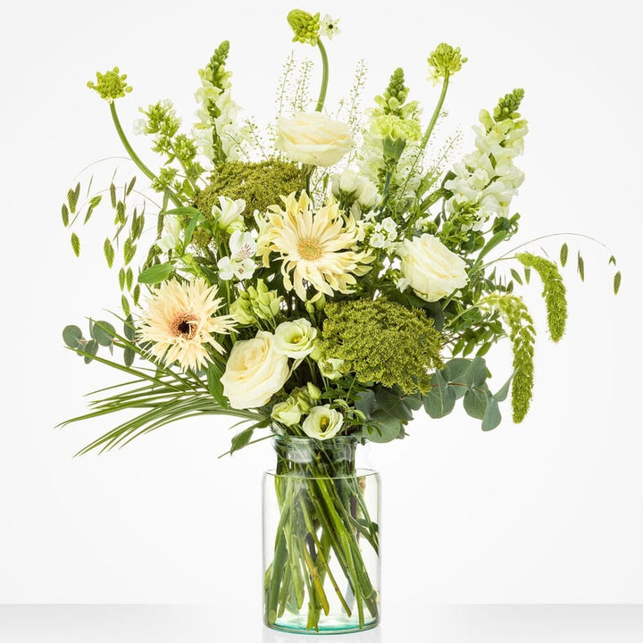 Groot boeket met witte rozen, gerbera’s, snapdragons en groen blad in een glazen vaas.