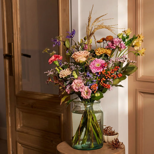 Najaarsboeket met kleurrijke bloemen in een glazen vaas, sfeervolle herfstdecoratie.