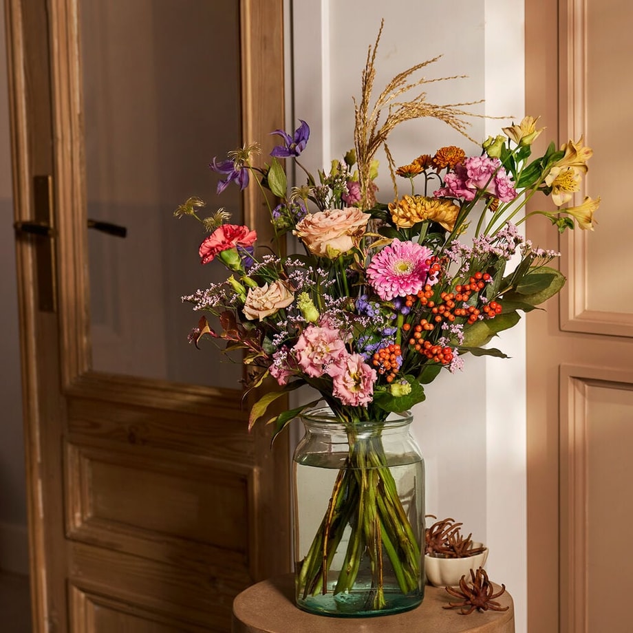 Najaarsboeket met kleurrijke bloemen in een glazen vaas, sfeervolle herfstdecoratie.