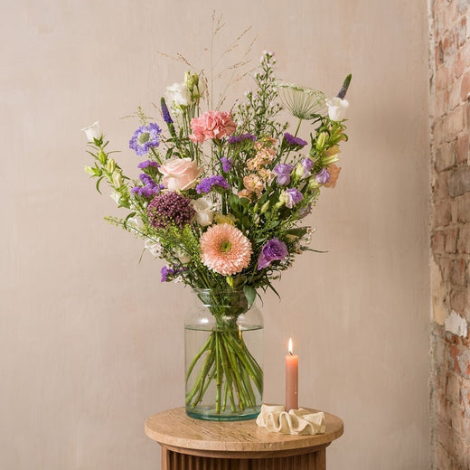 Veldboeket in zachte pastelkleuren met rozen, gerbera en lisianthus in glazen vaas.