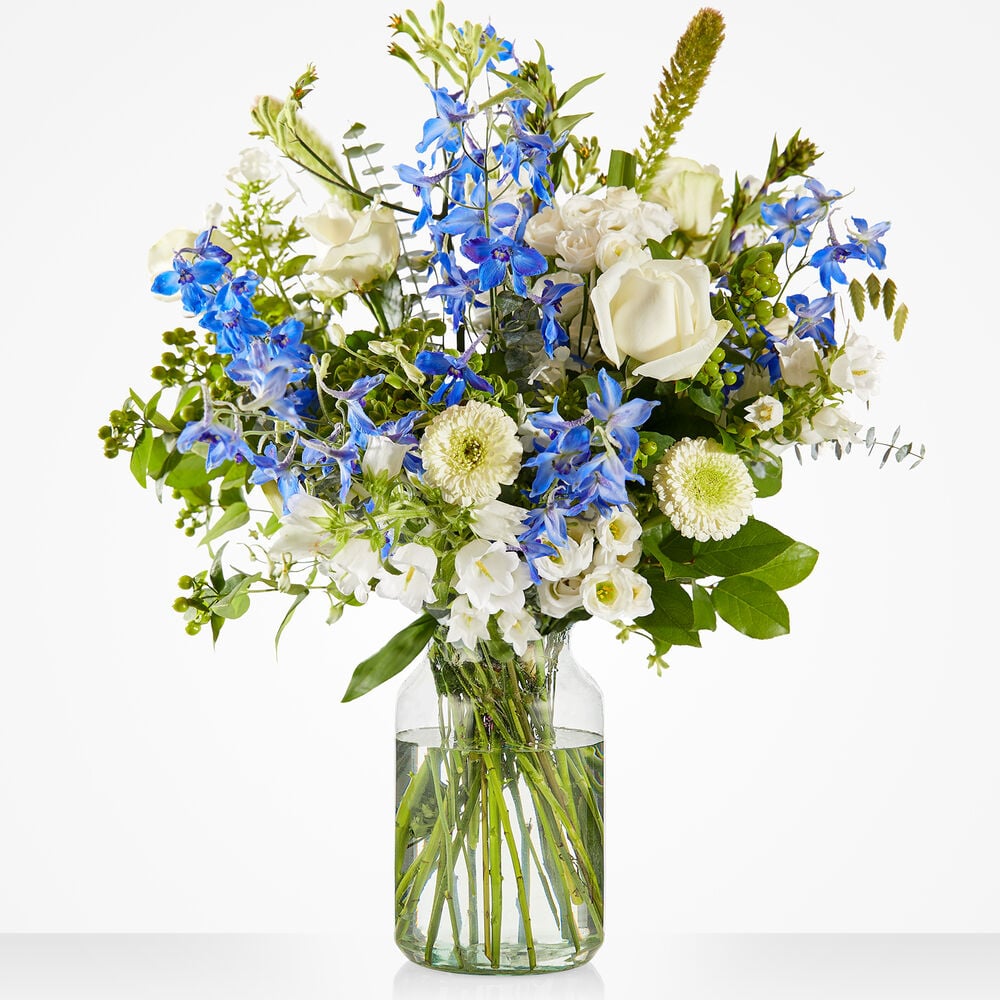 Sterkte boeket met witte en blauwe bloemen, waaronder rozen en delphinium, in glazen vaas tegen witte achtergrond