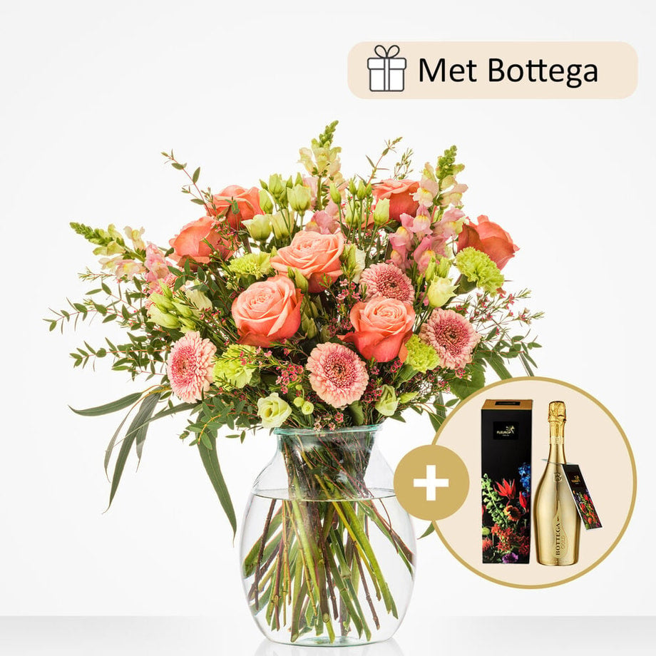 Groot boeket in een glazen vaas, met oranje rozen, roze gerbera’s, groene bladeren, en andere bloemen, samen met een fles Bottega wijn.