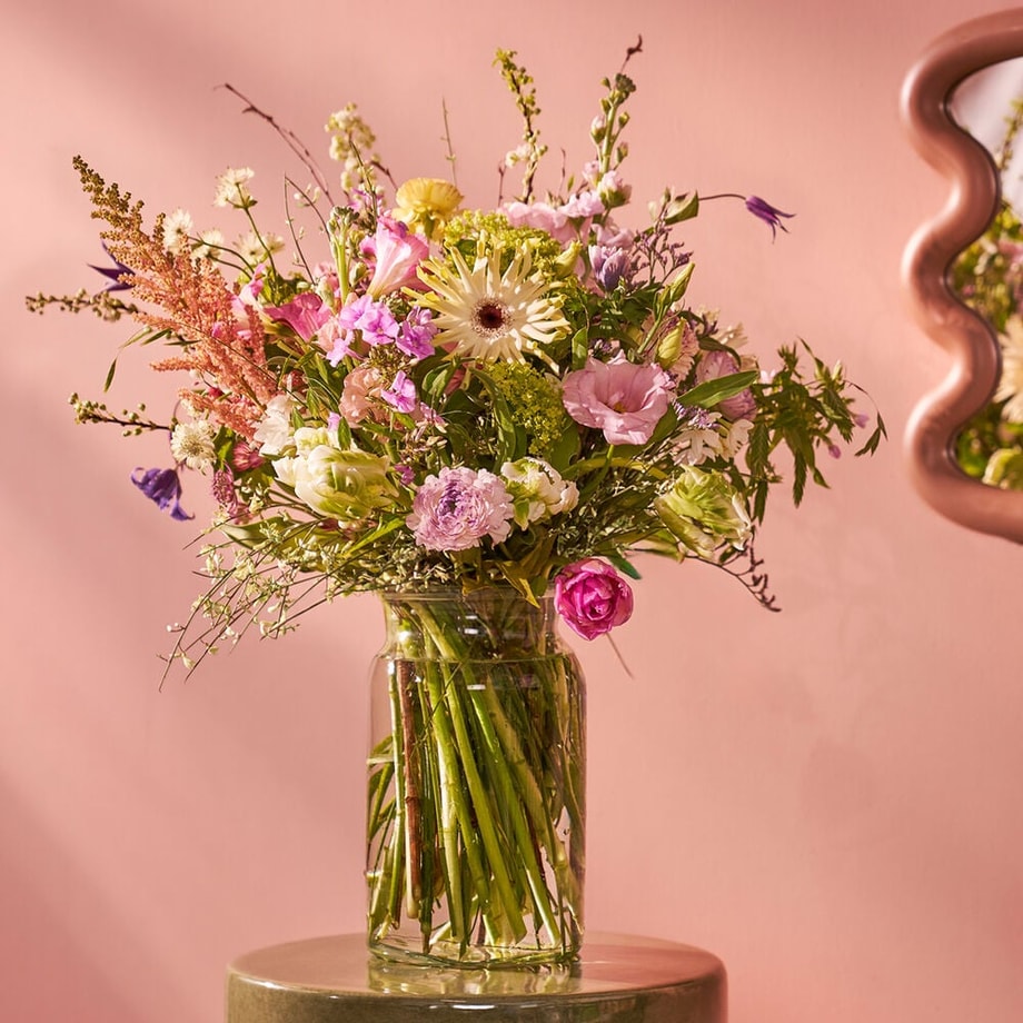 Uitbundig voorjaarsboeket in vaas op tafel in sfeervolle setting met roze muur