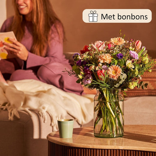 Kleurrijk rond seizoensboeket in vaas op tafel naast een vrouw met een kaart.