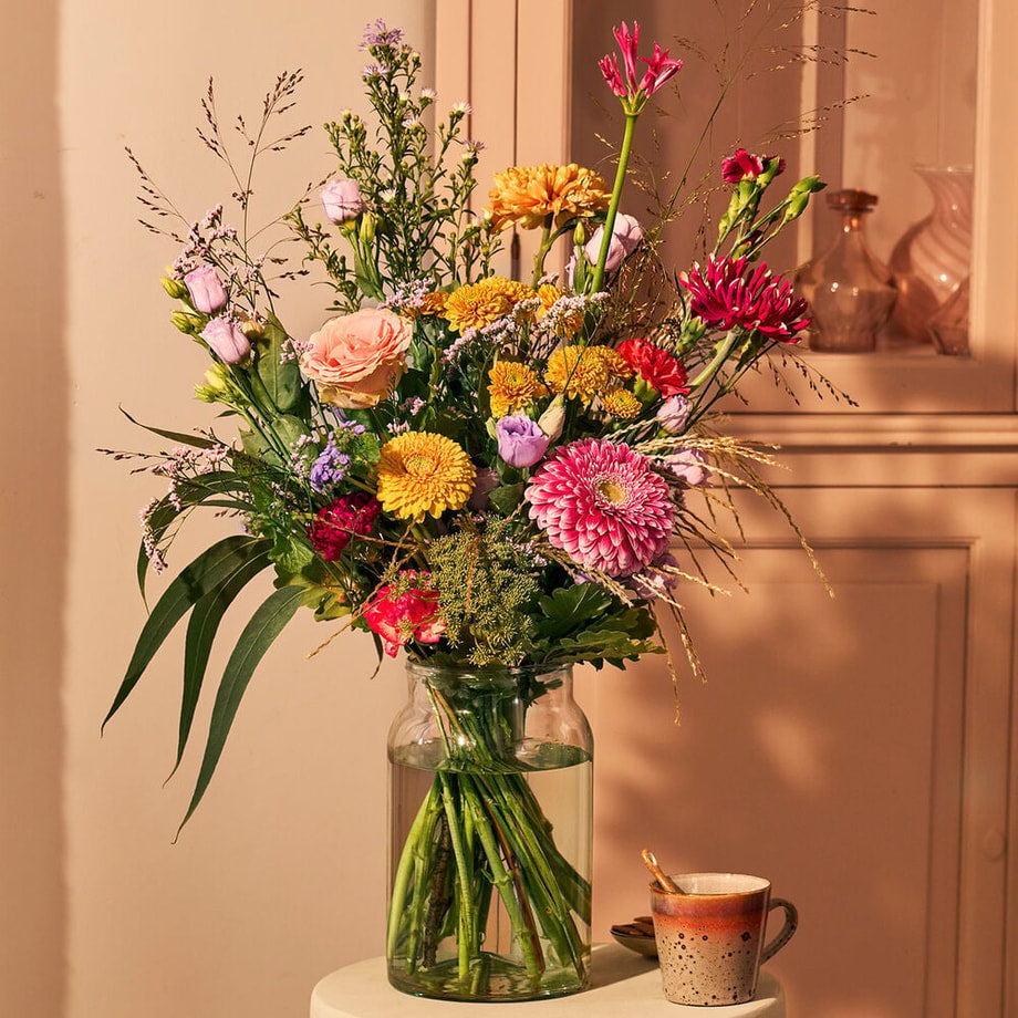 Boeket vol kleur met dahlia’s, rozen en seizoensbloemen in een glazen vaas, warme interieurdecoratie.