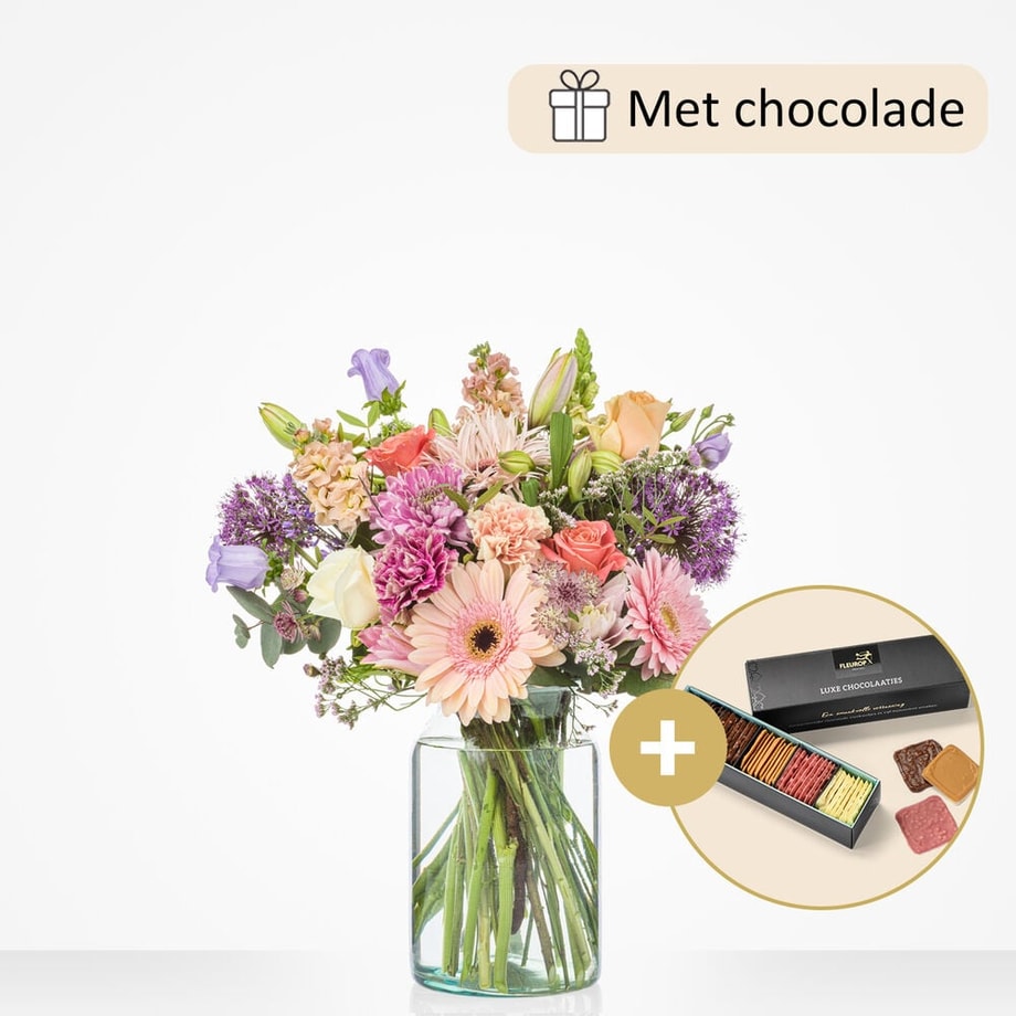 Groot boeket in een glazen vaas met een mix van bloemen zoals gerbera’s, rozen, lila bloemen, en lelies, gepresenteerd met een doos luxe chocolade.