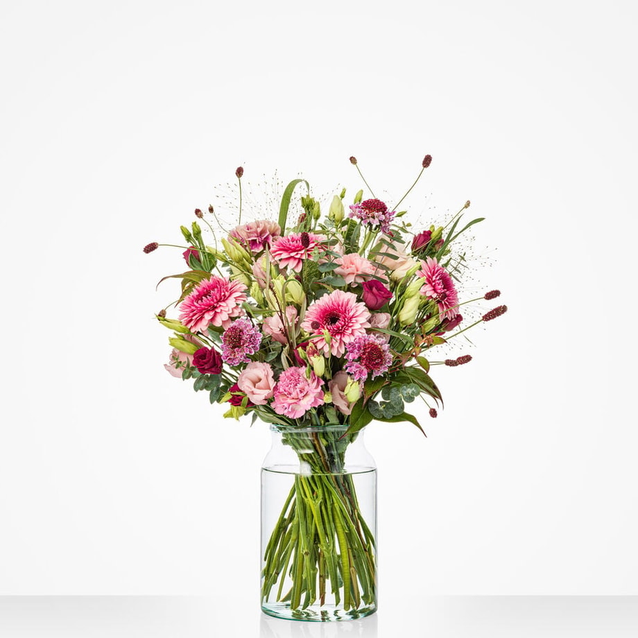 Groot boeket met roze, paarse en lila bloemen in een glazen vaas, op witte achtergrond