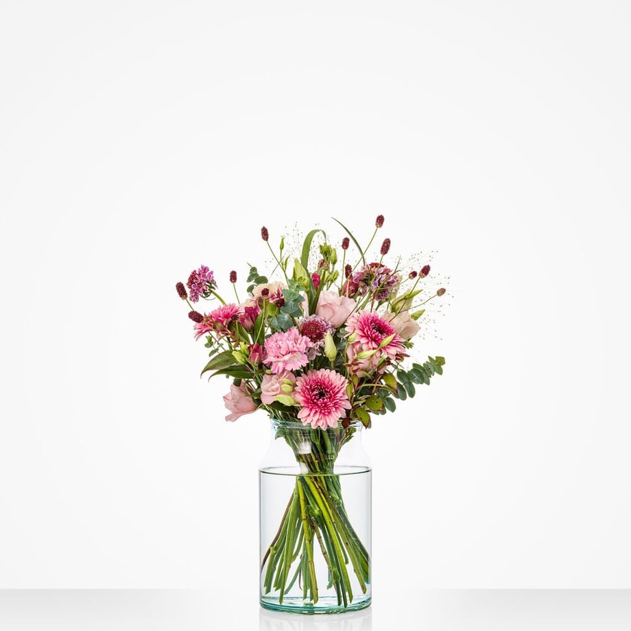 Klein boeket met roze en paarse bloemen in een glazen vaas, geschikt voor Moederdag