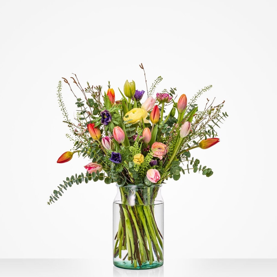Middelgroot voorjaarsboeket met kleurrijke bloemenmix in glazen vaas