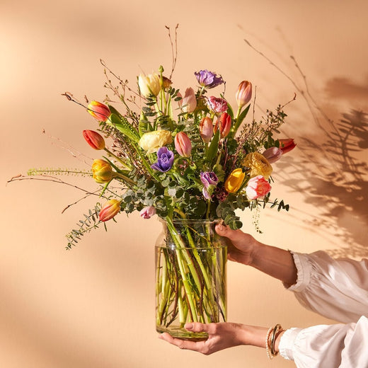 Vrolijk voorjaarsboeket in vaas vastgehouden tegen warme achtergrond