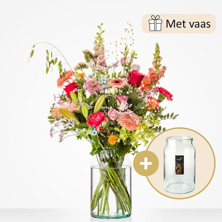 Groot boeket met een rijke mix van bloemen zoals rode rozen, gele lelies, roze gerbera’s, leeuwenbekjes en anjers, in een grote glazen vaas.