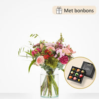 Klein boeket in een glazen vaas met roze rozen, rode alstroemeria, groene bolvormige bloemen, roze gerbera’s en paarse anjers, geleverd met een doos luxe bonbons.