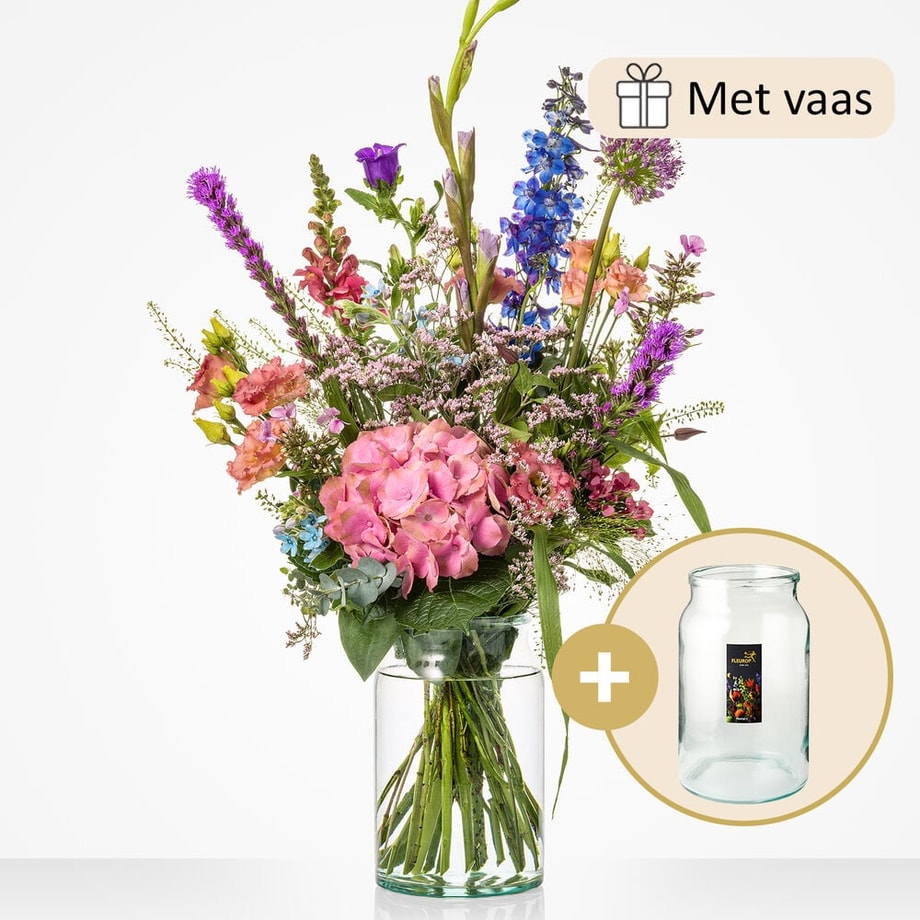 Middelgroot boeket met een mix van bloemen zoals roze hortensia’s, paarse riddersporen, leeuwenbekjes, en lila bloemen, geleverd met een bijpassende glazen vaas.
