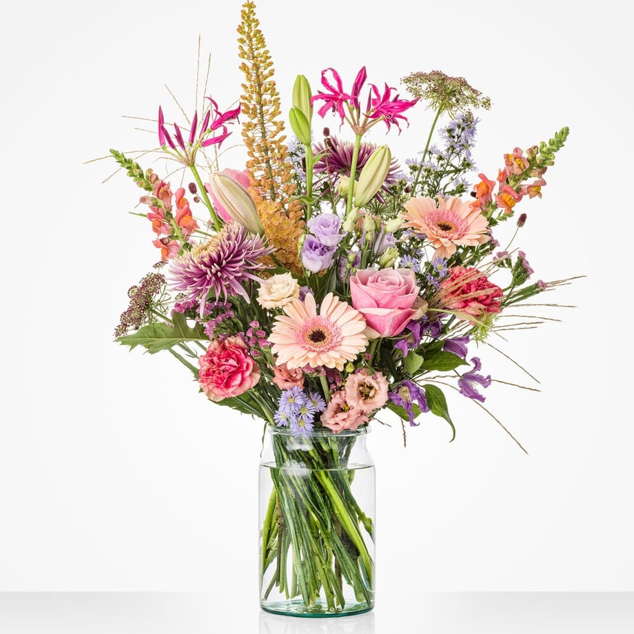Groot boeket in een glazen vaas met een mix van kleurrijke bloemen, waaronder roze gerbera’s, lelies en lichtpaarse bloemen.