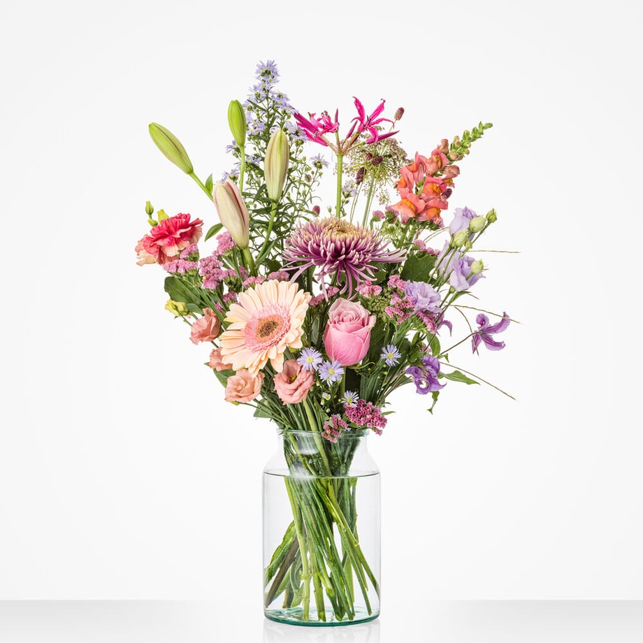 Klein boeket in een glazen vaas met een mix van kleurrijke bloemen, waaronder roze gerbera’s, lelies en lichtpaarse bloemen.