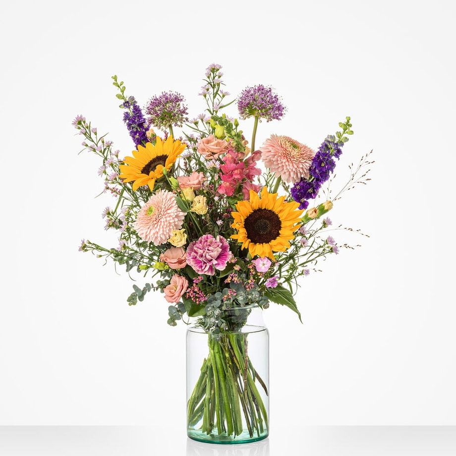 Middelgroot boeket in een glazen vaas met een mix van kleurrijke bloemen, waaronder zonnebloemen, roze en paarse bloemen.